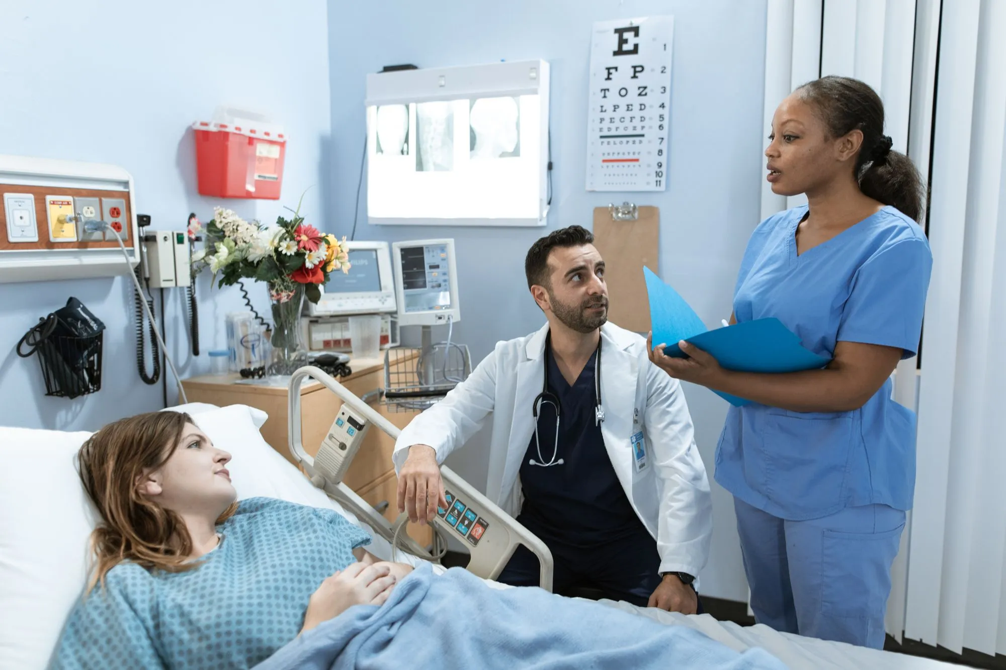 A doctor and nurse reviewing a chart beside a patient bed